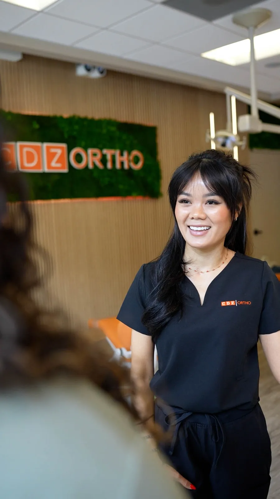 Dr. Cen standing by the CDZ Ortho logo wall